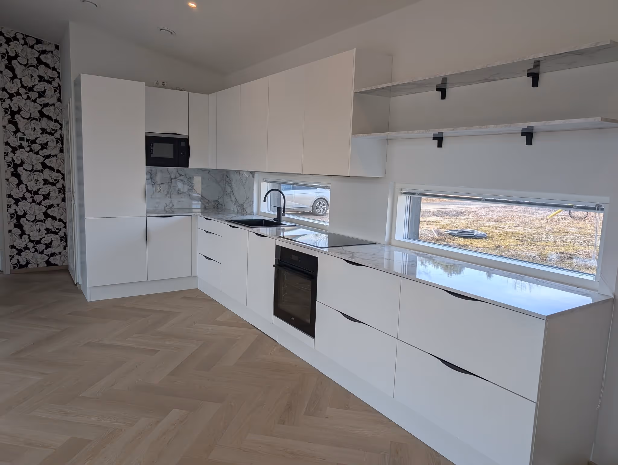 Moderni keittiö valkoisilla kaapistoilla, marmoritason tasoilla ja kaksilla suorakaiteen muotoisilla ikkunoilla.